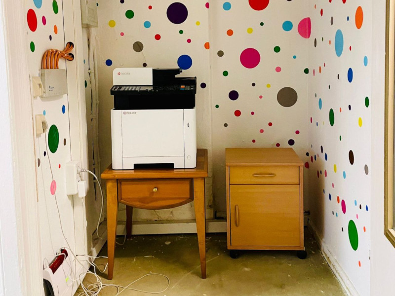 a white printer on a little brown table in front of a white wall with colourfull polko dots