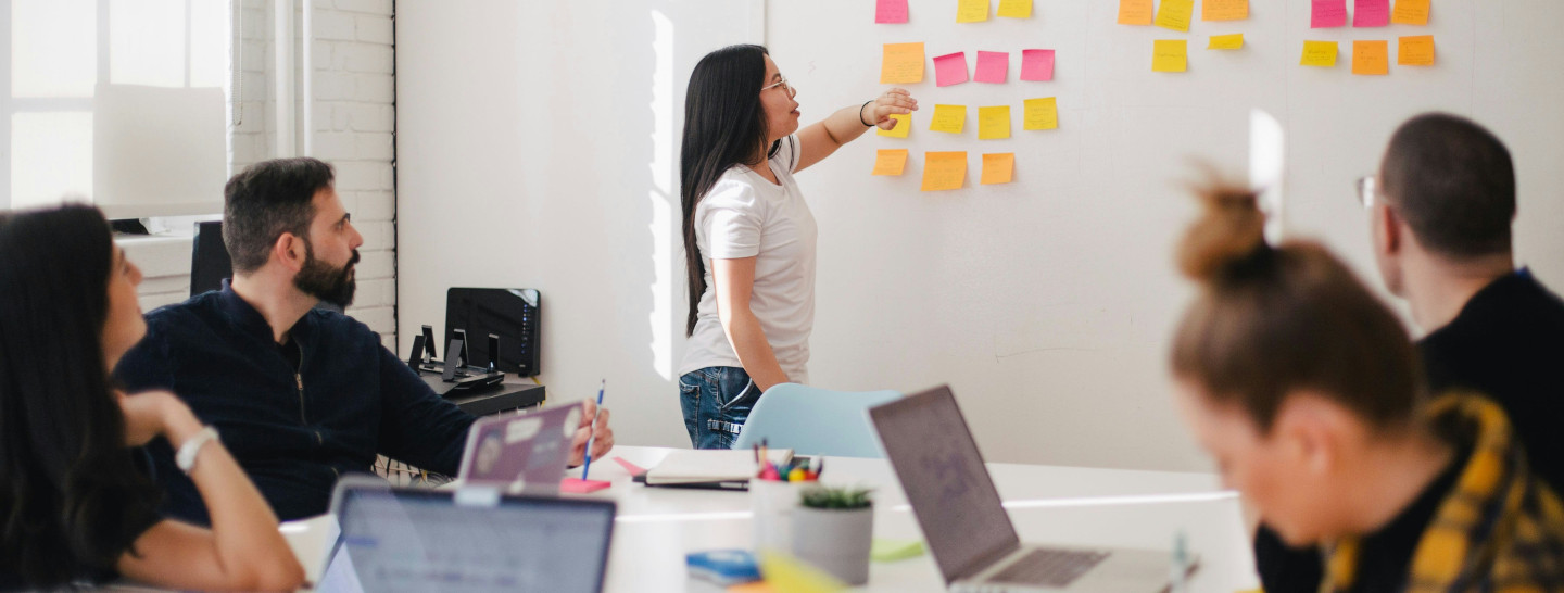woman putting post-it on wall in a room with colleagues